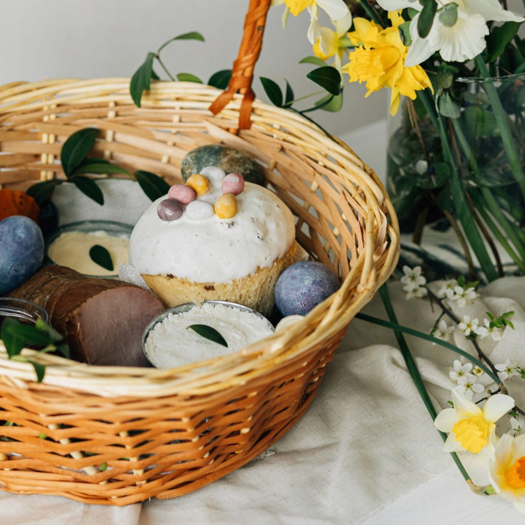 Happy Easter! Stylish easter basket with natural dyed eggs, meat, bread, butter, beets and spring flowers on rustic table. Traditional easter orthodox holiday food and daffodils bouquet