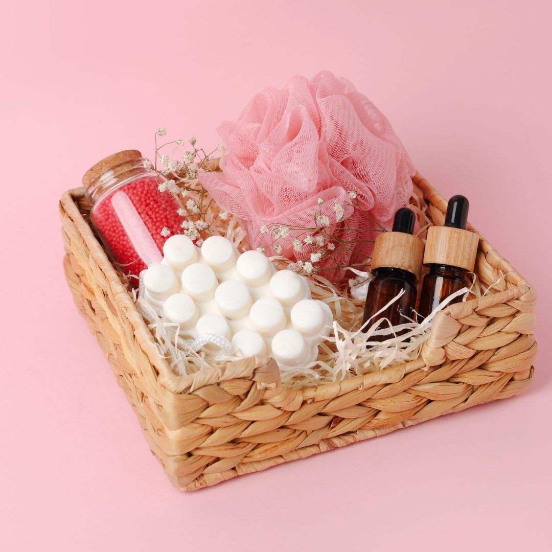 Spa gift set of different luxury products in wicker basket on pale pink background