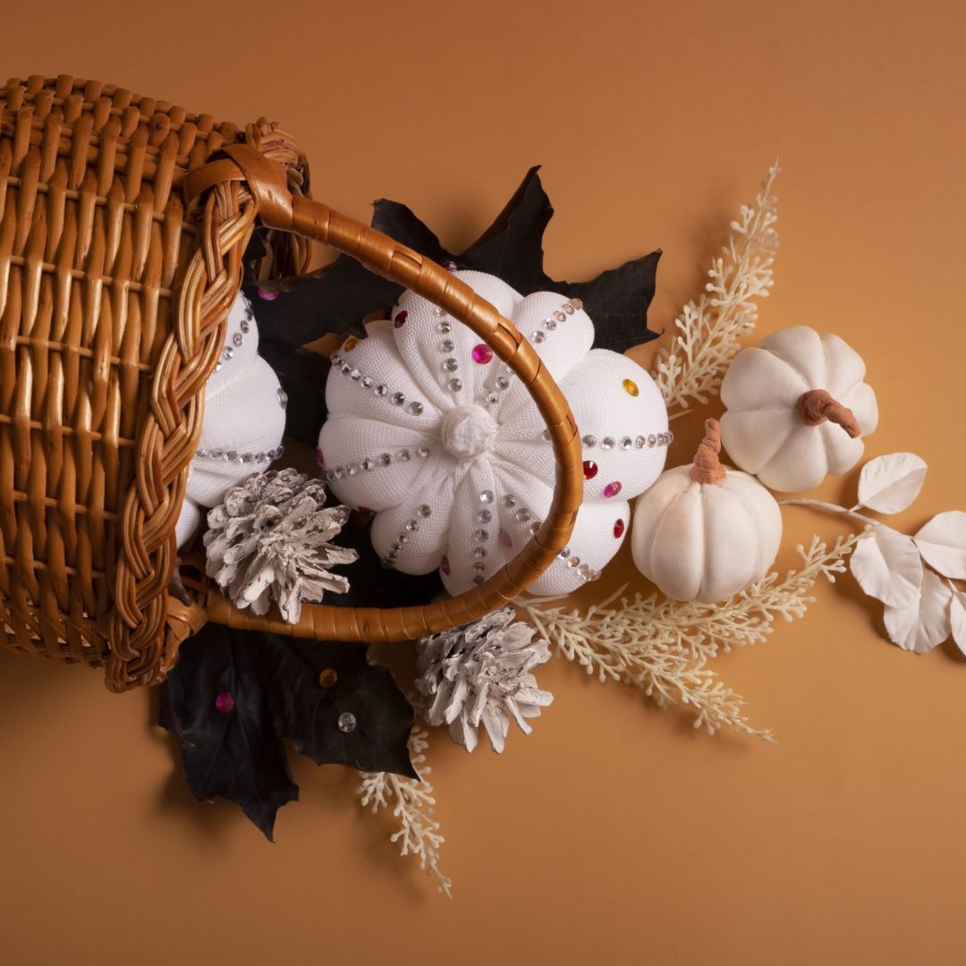 White decorative textile pumpkins with shiny stones and pine cones with basket on colored background. Autumn harvest concept.